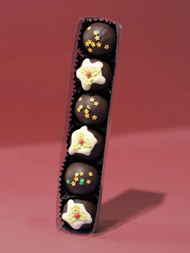 A tube of 6 dark chocolate Christmas truffles, 3 decorated with edible stars and 3 decorated with white chocolate and a holly leaf.