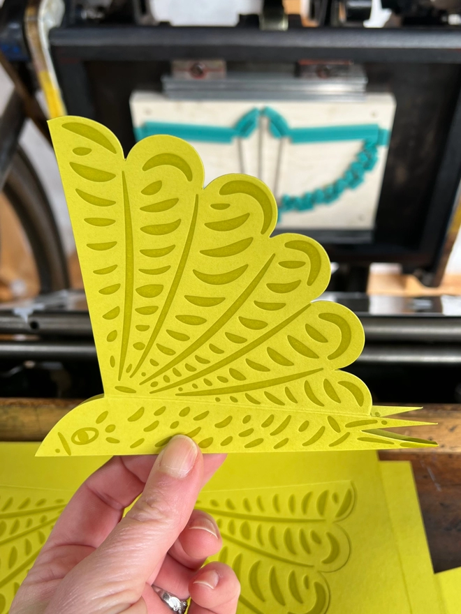 Letterpress printed bird decoration being held in front of printing press with die-cut shape.