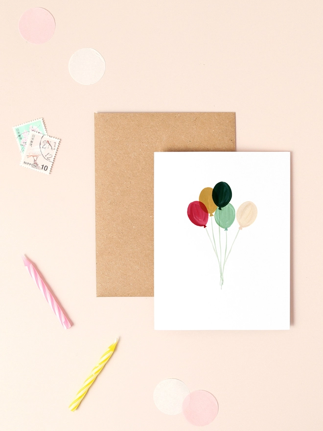 A vibrant illustration featuring a cluster of colorful balloons in shades of red, yellow, green, and blue, floating against a soft, neutral background. The balloons are depicted in a loose, hand-painted style, conveying a sense of lightness and celebration. The design is minimalist and cheerful, perfect for conveying joy and well wishes.
