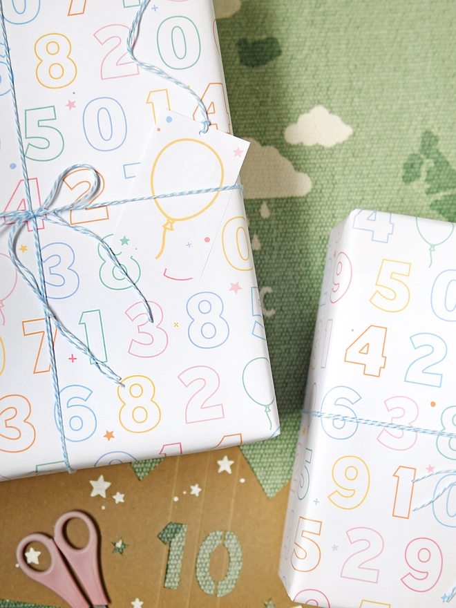 A birthday gift wrapped in colour-in numbers wrapping paper lays on a green rug.
