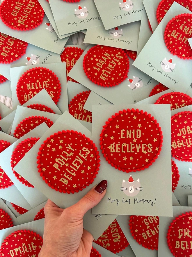 Red christmas 'Believe' badges with gold stars and a red pom pom trim and a child's name 