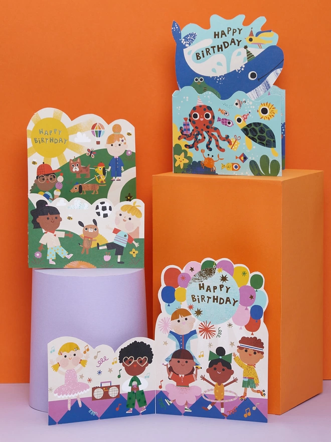 Other cards from the Raspberry Blossom ‘Fantabulous’ children’s greeting card collection. Grouped together on lilac plinths and with an orange background, the colourful birthday cards include fun disco, underwater, and park themes