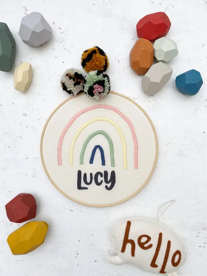 personalised name and rainbow embroidered hoop. cotton hoop embroidered with the name lucyand a pink, yellow and blue rainbow.
