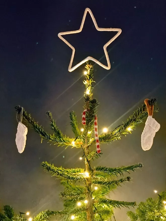 Top of a decorated Christmas tree topped with a large string covered wire star against a grey wall