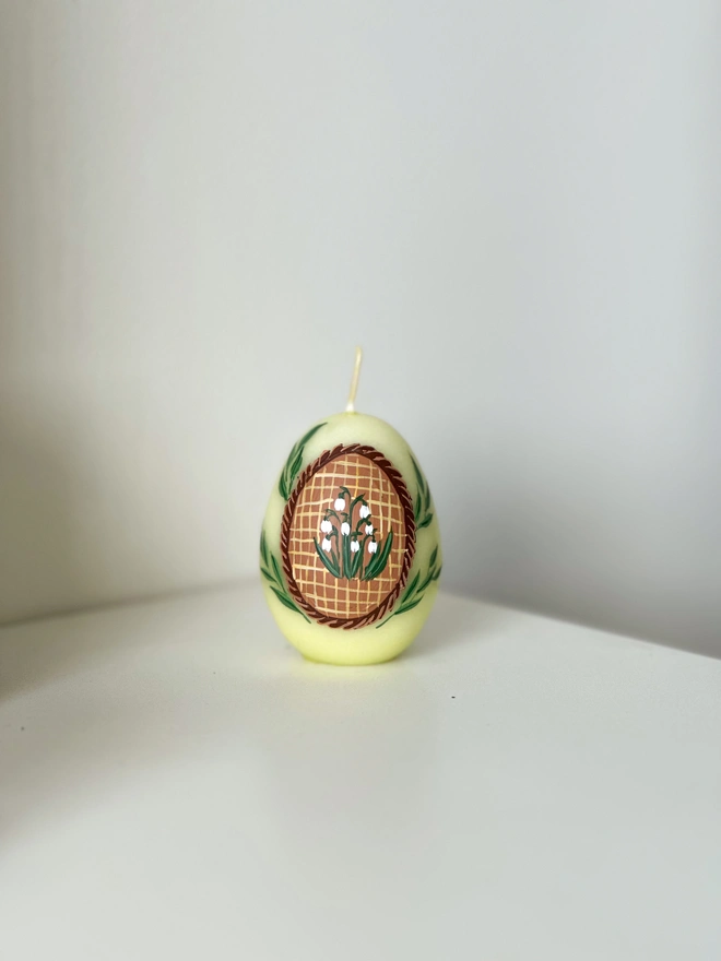 Hand Painted Easter Egg Candle Snowdrops, an Easter egg candle sitting on a plain surface. It's Easter and floral design wraps around it. 