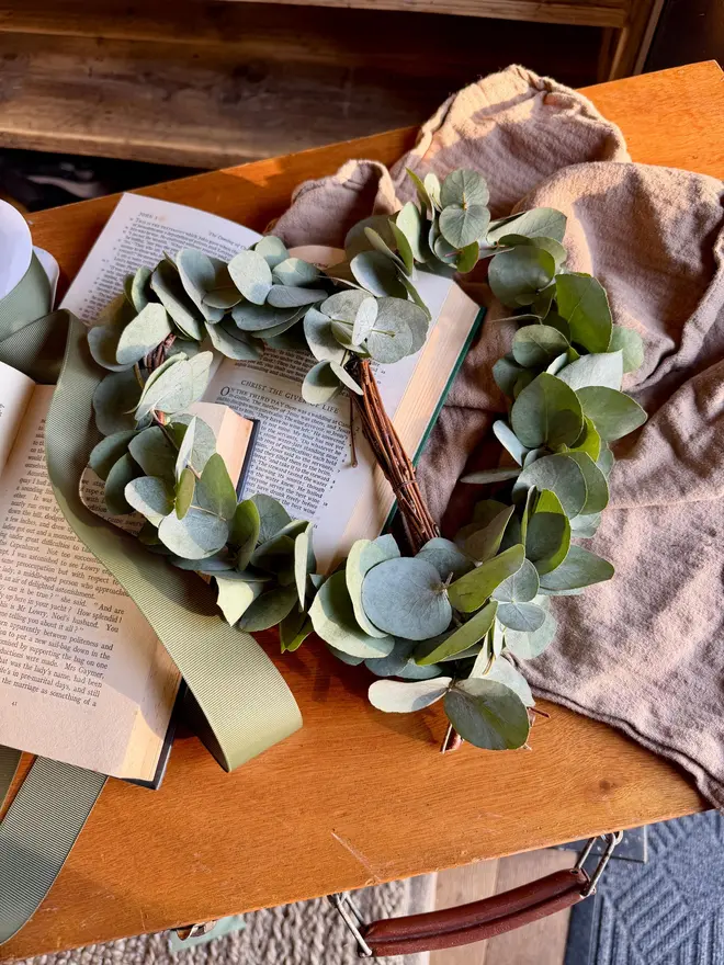 A frame of birch woven with sprigs of fresh eucalyptus. The leaves are a soft, muted green with a slightly silvery tone, round in shape. They cluster gently rather than covering the whole heart, so you can still see the wooden structure underneath.