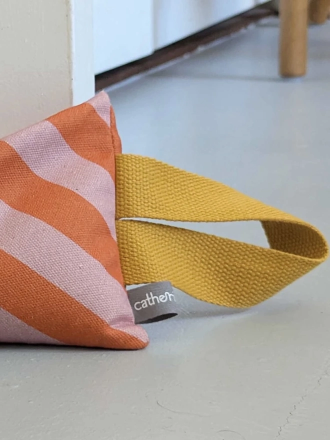 Draught Excluder, a colourful patterned draught excluder sitting on the floor by a white door. 