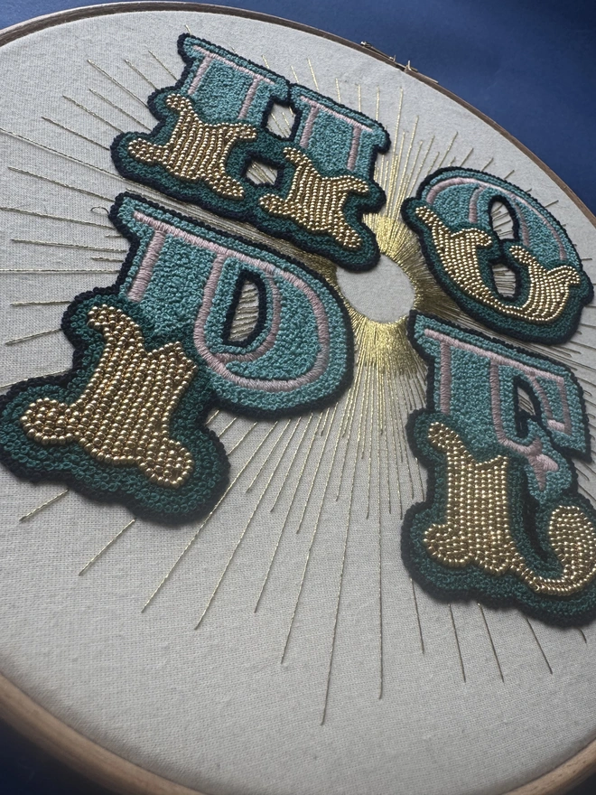 A close up of an embroidery hoop containing the hand sewn word Hope stitched in greens and gold  beads 