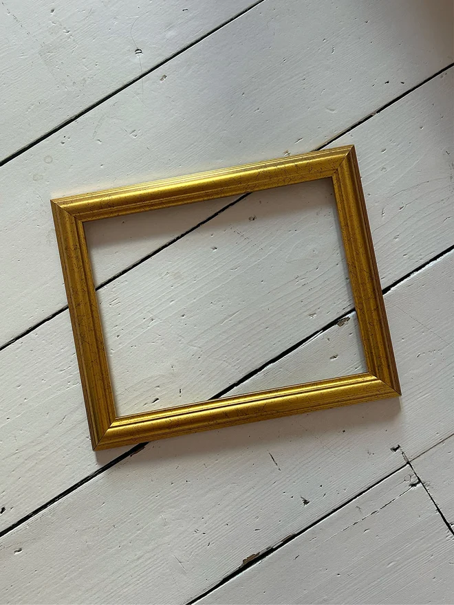 a gold antique effect frame on a white floorboard background