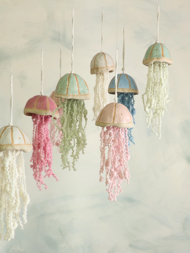 multicolour handmade ceramic jellyfish decorations hang against and swirly blue and white background