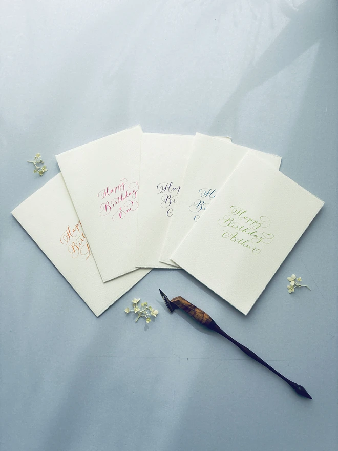 collection of calligraphy cards in colourful ink shown with a calligraphy pen