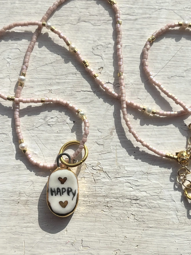 pink bead necklace, with white and gold pendant with the inscription Happy