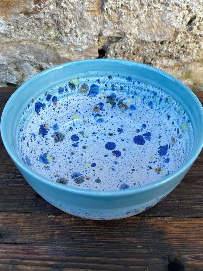 Shoreline Small Bowl, a colourful bowl placed on a wooden surface in front of a brick wall. 