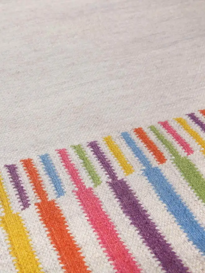 Rainbow Border Flatweave Rug, a rainbow rug sitting on top of a grey surface. 