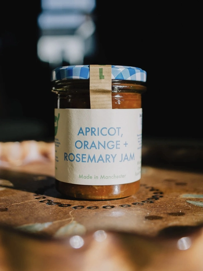 Jar Of Apricot, Orange & Rosemary Jam, jar of jam with a blue lid on a decorated plate on a table. 