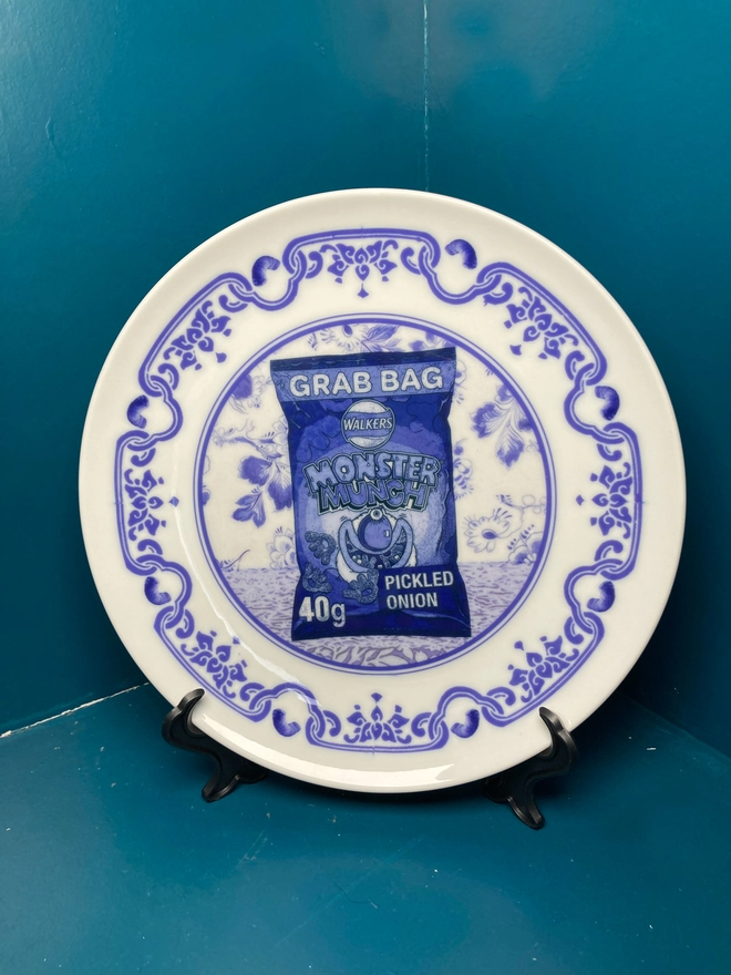 An 8" blue and white 'Delft' style plate featuring a packet of Monster Munch