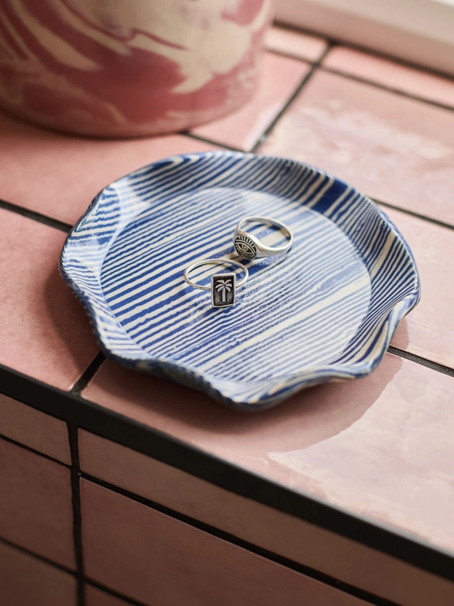 Striped Trinket Dish, a colourful trinket dish on a window sill. It is accompanied by some rings. 