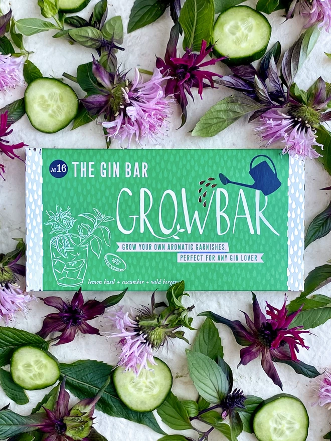 The Gin Growbar surrounded by pink and purple bergamont flowers, cucumbers and lemon basil leaves. 