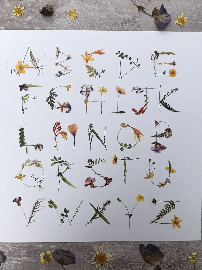 Alphabet Print Of Real Pressed Wildflowers, a print of the alphabet with pressed flowers on a wooden surface. 