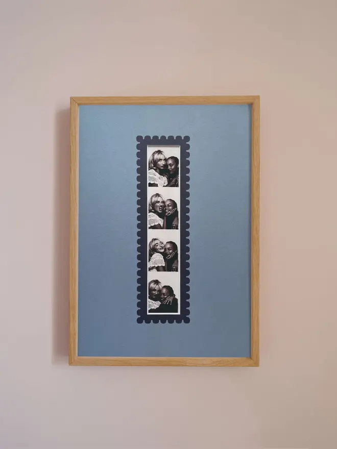 Oak A4 picture frame with a blue mount and scalloped border, displaying a centered vertical photo booth strip, hung on a neutral beige wall.