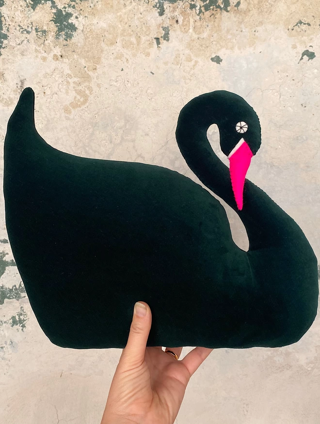 A hand holds a green swan  with a pink beak
