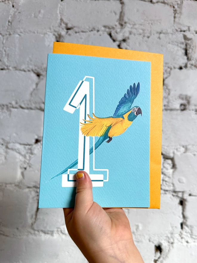 a bright blue card with a big white number 1 and an illustration of a macaw with a yellow envelope
