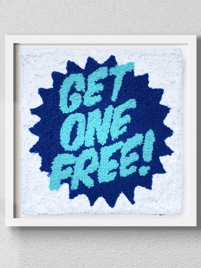 get one free written in cyan on a dark blue start and white woollen background mounted in a square white box frame on a grey wall