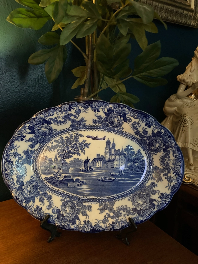 Classic blue and white patterned plate featuring a castle and river with boats sailing along. A Jet2 plane flies high in the sky.