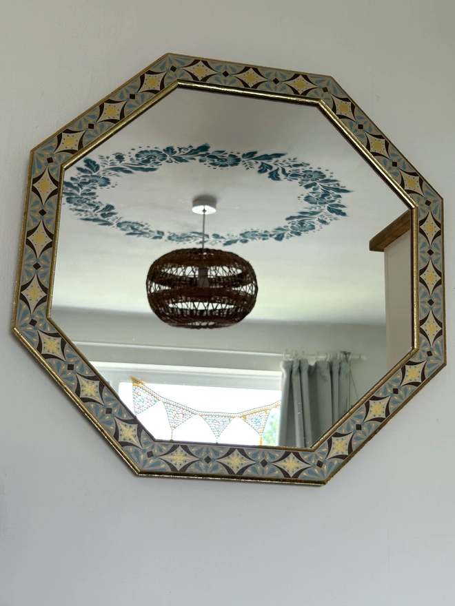 Medium sized octagonal wall mirror with a hand painted decorated frame with gold stars and blue star burst repeating pattern around the frame