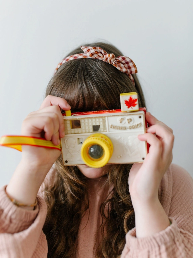 Girl in check gingham Alice Band and vintage toy camera