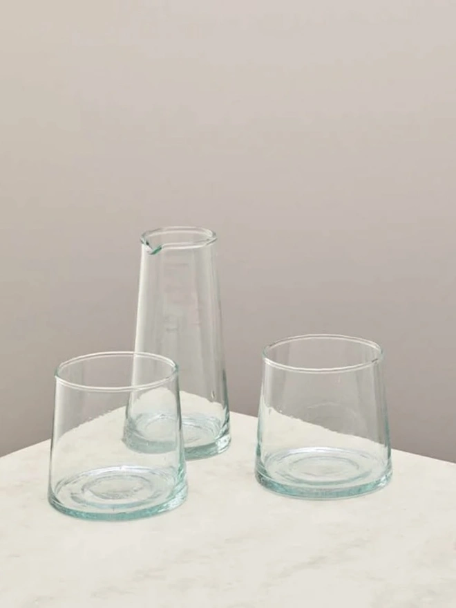 Whisky Glasses (Set Of 3), a set of whisky glasses and a jug sitting on a plain counter top against a grey backdrop. 