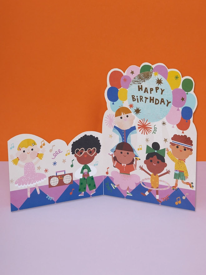 A disco birthday party themed die cut children’s birthday card, filled with colourful balloons and party guests dancing away. The card is complete with gold foil details and a gold foil ‘Happy Birthday’ message