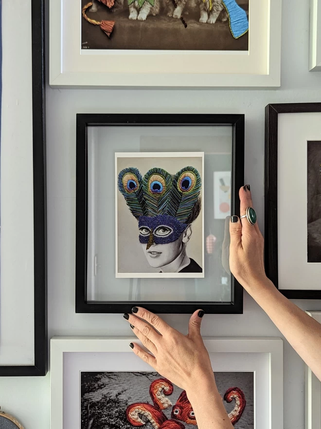 Embroidered peacock mask print held in frame on wall 