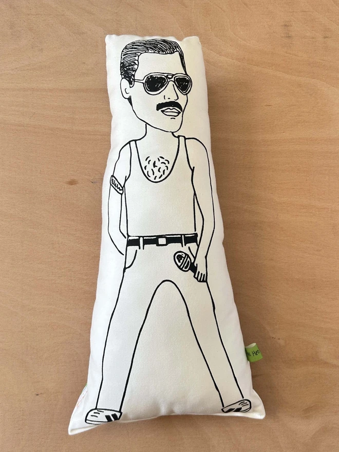 Black and white illustrated screen printed cushion of Queen frontman Freddie Mercury. The cushion sits on a light wood surface.