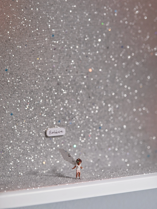 Miniature scene in an artbox showing a tiny fairy figurine standing against a sparkling pinky silver backdrop 