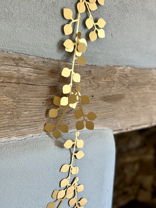 Gold Laurel Berry Paper Garland hung vertically, paper decorations reflect the sunlight
