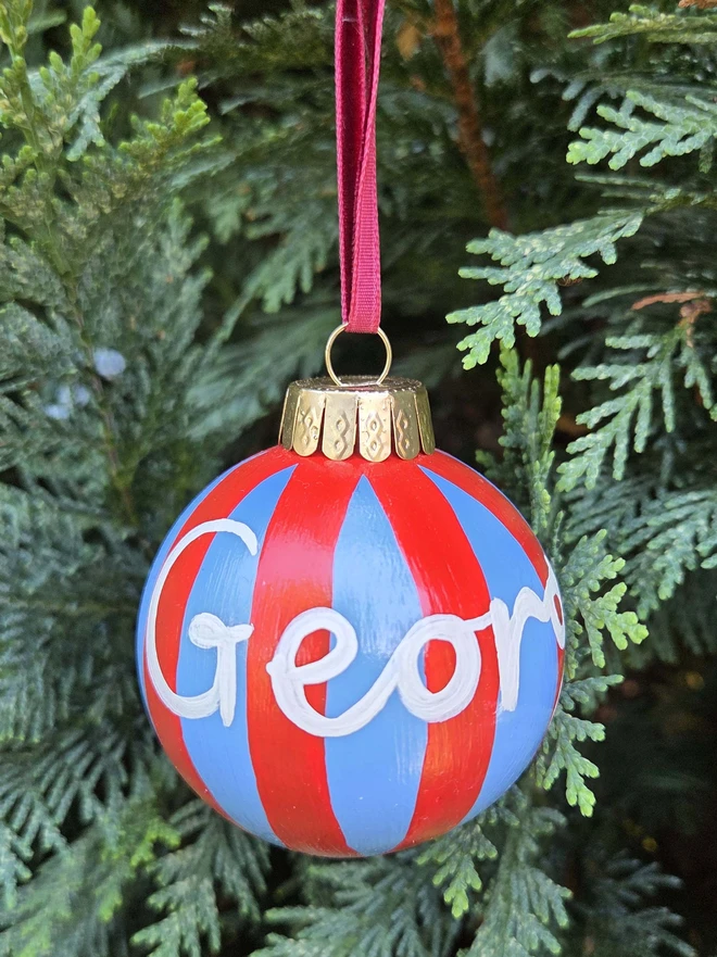 hand painted blue and red stripe bauble with name personalisation, hanging on a christmas tree