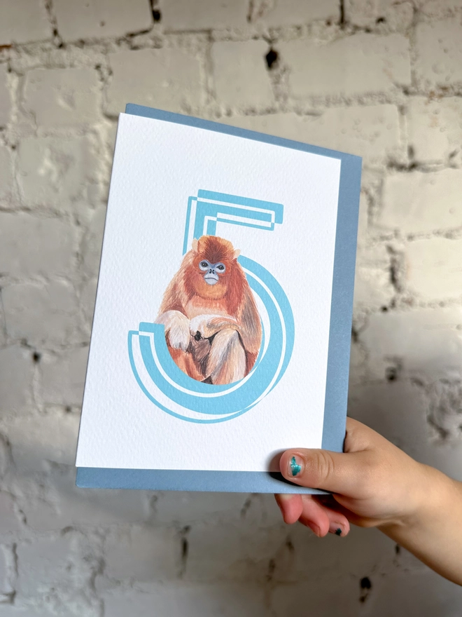 a white card with a big blue number 5 and a snub nose monkey illustration and a blue envelope