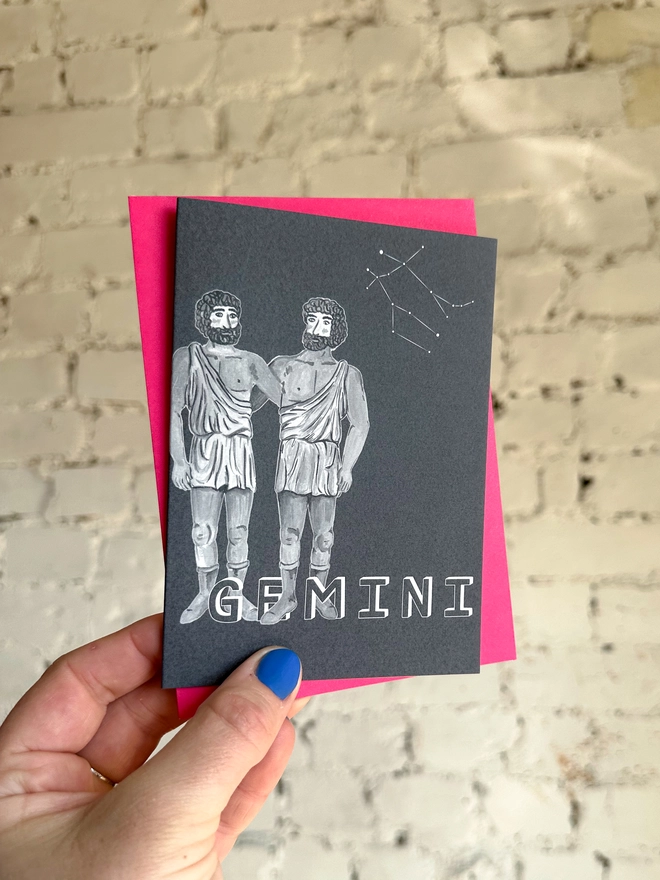 a greetings card featuring a greyscale illustration of a zodiac style twins with the text “GEMINI” with a neon pink envelope