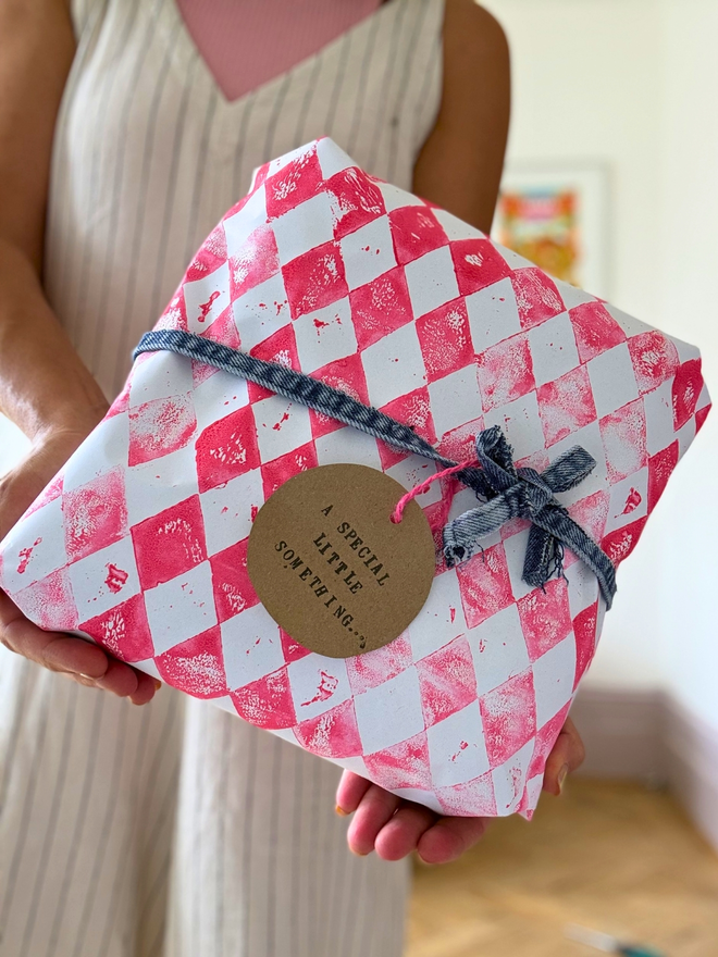 Gift wrapping in a pink handprinted harlequin print paper with a denim bow and gift-tag