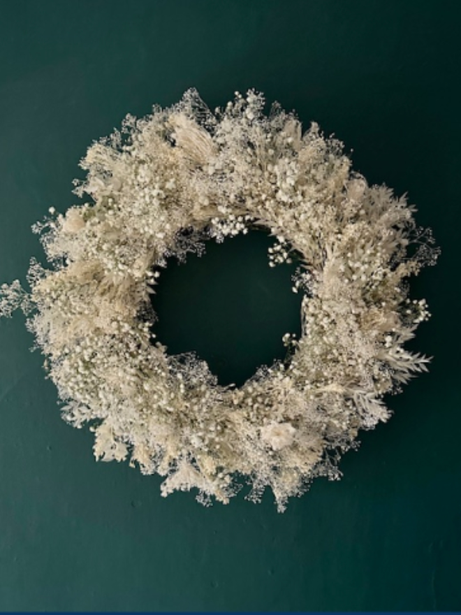 dried floral white door wreath. a circular white and green wreath made of dried flowers hung on a forest green wall.