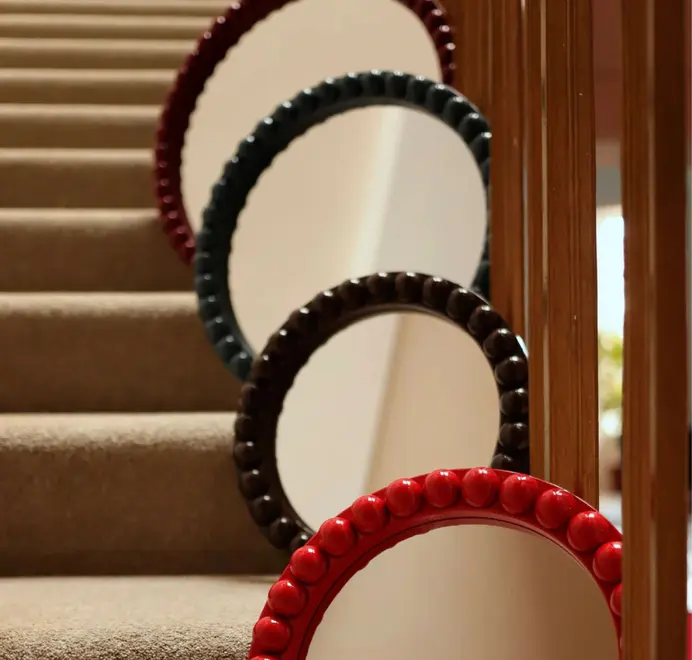 Many round oversized bobbin mirrors, in different colours, decorative bobbin-style wooden frame arranged on stairs. 