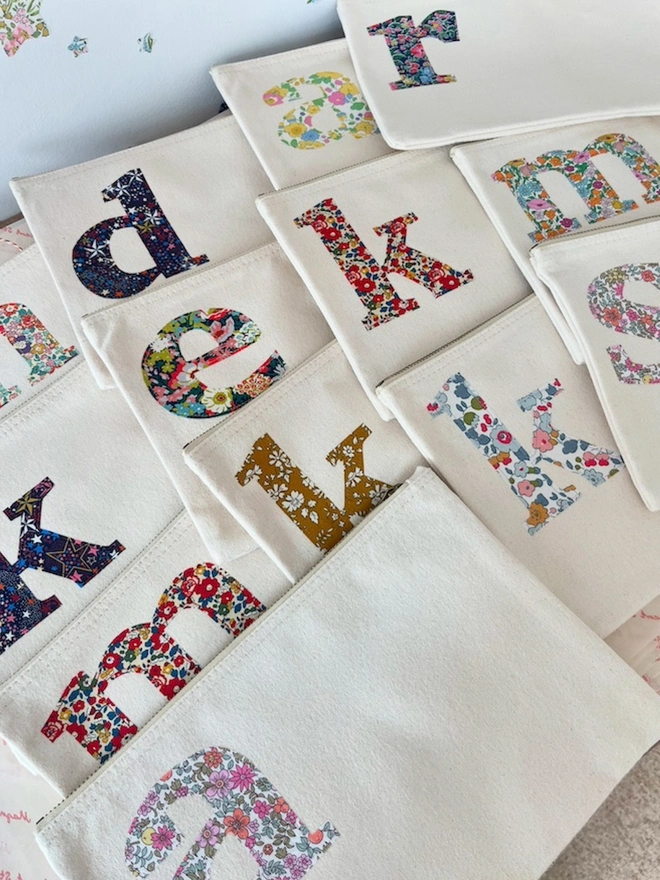 a collection of natural make up zip up pouches personalised with a liberty print initial on the front in the corner