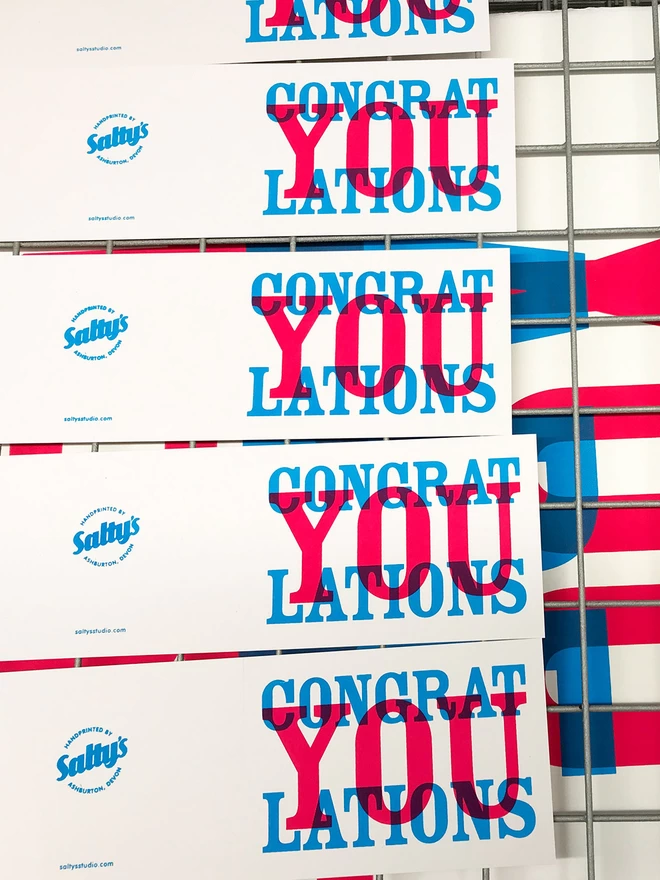 Ariel view of the drying rack showing many Congratulations in magenta and cyan ink, cards drying next to each other.