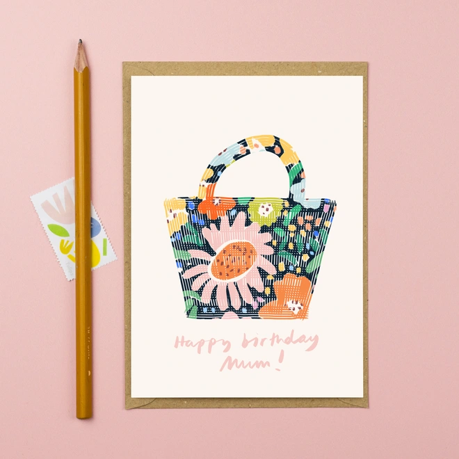 A greetings card featuring a floral shopping bag with the words Happy birthday mum in pink handwritten font underneath.