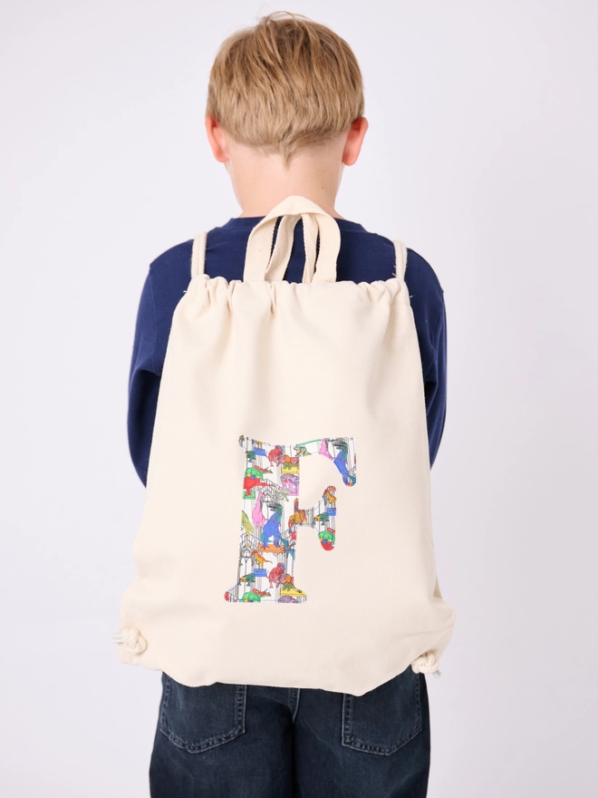 a 5 year old boy wearing a Magnificent Stanley Personalised Liberty Print Drawstring Backpack with his initial on in dinosaur print