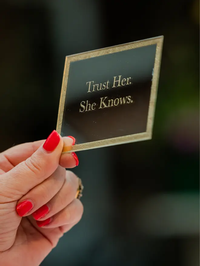 'Trust Her. She Knows' gold etched mirror held up by hand