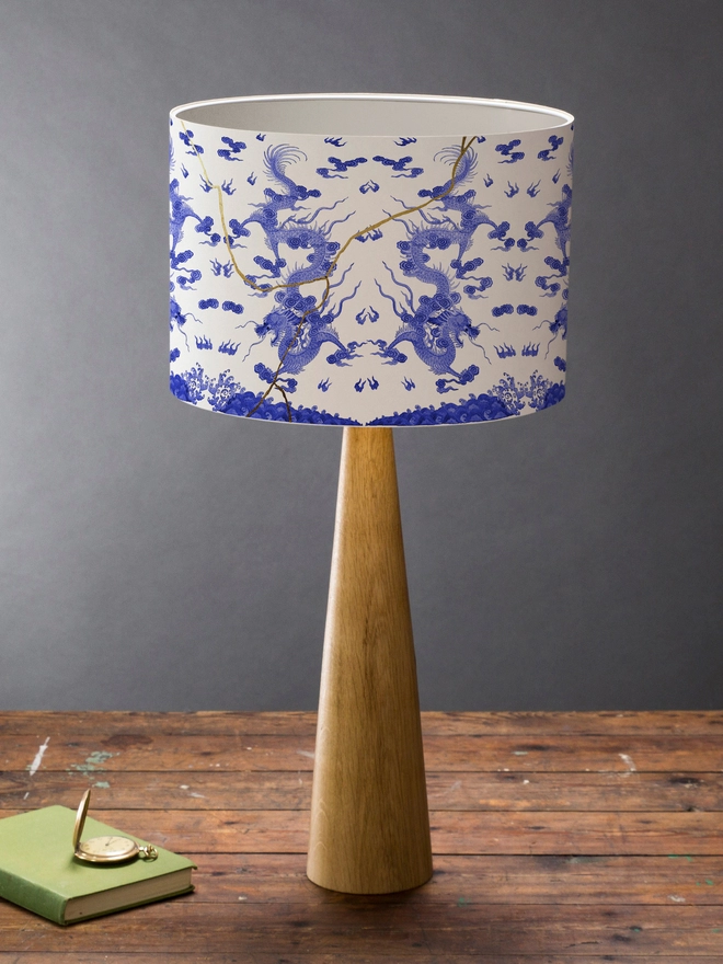 Drum Lampshade blue and white kintsugi inspired featuring Japanese dragons on a wooden base on a shelf with books and ornaments