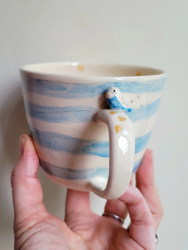 Handmade blue stripey budgie bird mug held in a hand