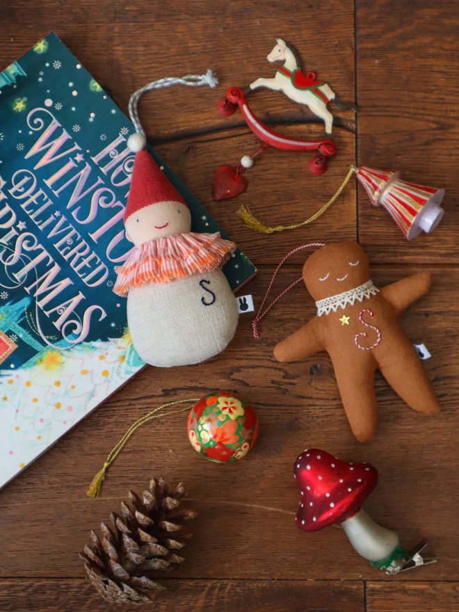 Brown linen gingerbread man christmas tree ornament with a letter hand embroidered in candy cane colours, star shaped sequin, crochet cotton lace around the neck, smile embroidered in white and candy cane colour string to hang. 